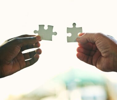 Two hands holding connecting two puzzle pieces.